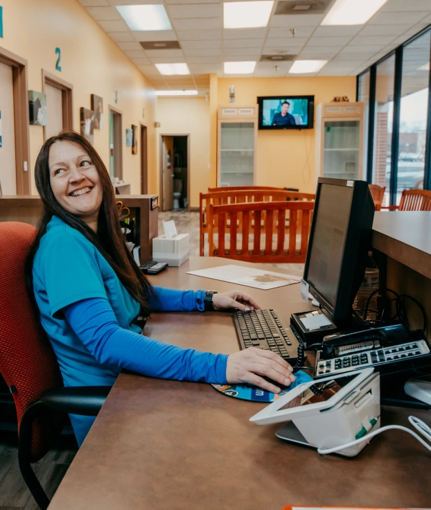 Veterinary receptionist smiling while working at the front desk of a veterinary clinic.