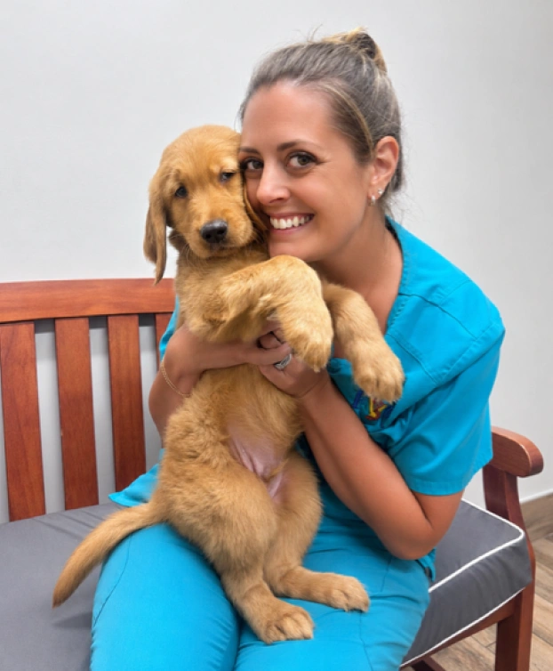 Smiling veterinary staff member in teal scrubs holding a golden retriever puppy