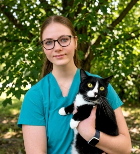 Staff member in teal scrubs holding a black and white cat outdoors