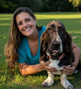 Staff member in a teal top lying in grass with a Basset Hound outdoors